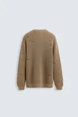 Sweater color marrón claro de punto con cuello redondo y manga larga. Presenta roturas en toda la prenda y terminaciones irregulares.