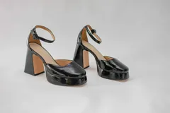 Zapatos de tacón alto con plataforma, color negro charol, con correa al tobillo y hebilla. Capellada, forro y plantilla 100% de cuero. Tacón de 10 cm.