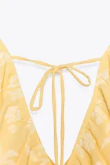 Top amarillo con estampado floral en jacquard, escote en pico, mangas cortas abullonadas con elástico, cintura elástica y espalda descubierta ajustable con lazos.