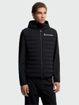 Chaqueta híbrida Moncler Grenoble negra con cuerpo acolchado y mangas de tejido liso. Presenta capucha fija, cierre frontal y logo de Moncler Grenoble en el pecho izquierdo.