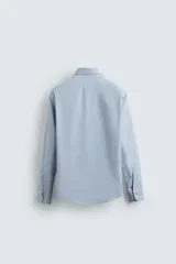 Camisa celeste con finas rayas verticales blancas, de corte regular, cuello italiano, manga larga con puños abotonados y cierre frontal con botones.