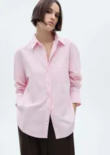 Camisa rosada de algodón con corte recto, cuello camisero, manga larga con puños abotonados, bolsillo de parche en el pecho y cierre frontal con botones.