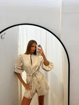 Mono corto de lino color beige claro, con cuello mao, cierre frontal, mangas globo largas y cinto para ajustar a la cintura.