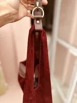 Cartera tipo hobo de gamuza color borgoña con flecos y asa corta de cuero marrón.