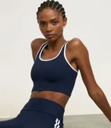 Top deportivo sin copa, color bordó, con escote en U y espalda tipo nadador. Presenta ribetes de color blanco en el contorno del escote y las sisas.