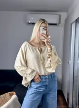 Blusa blanca de mangas largas con volados en los puños y escote con lazo.