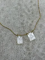 Collar dorado con cadena fina y dos dijes rectangulares con imágenes religiosas.