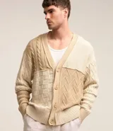 Cardigan de punto beige con diferentes texturas y bloques de color. Tiene cuello en V, abotonadura frontal y mangas largas.