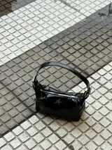 Cartera negra charolada con asa corta y cierre de cremallera. Tiene un aplique metálico en forma de estrella.