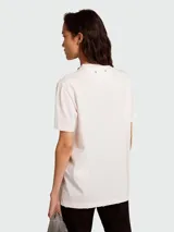 Remera de algodón color blanco roto, de corte holgado y manga corta con bordes deshilachados. Presenta un cuello redondo adornado con cristales cabujón engarzados.