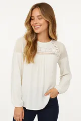 Blusa color marfil con detalles de encaje en el frente y los hombros, de mangas largas y corte holgado.