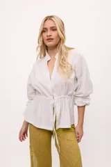 Chaqueta blanca de lino y algodón, con cuello mao, cierre frontal con botones y mangas largas con puños elásticos. Tiene cintura ajustable con cordón.