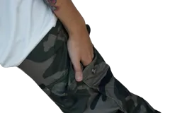 Pantalón cargo holgado con estampado camuflado en tonos verde militar, marrón y negro. Presenta cintura elástica ajustable con cordón blanco y bolsillos cargo laterales con cierre de botón a presión. Los tobillos son ajustables con cordones.