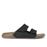Sandalias tipo slide de dos tiras ajustables con velcro, marca Reef. La capellada es negra y la suela es de goma EVA en color marrón claro. El nombre de la marca está grabado en relieve en la tira lateral.