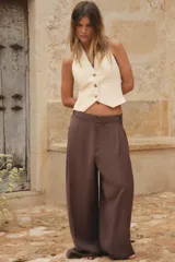 Pantalón marrón de tiro alto con trabillas, doble pliegue, bolsillos laterales y tapetas en la espalda. Pierna ancha y cierre frontal con cremallera y gancho metálico.