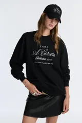 Gorra de béisbol negra de Zara con bordado frontal en blanco que dice "A Coruña Established 1975 Rúa Juan Flórez 64-66".