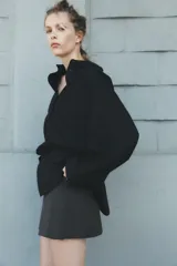 Camisa negra de cuello solapa y manga larga amplia. Tiene un bolsillo de parche en el delantero, detalle de pliegues y cierre frontal con botones.