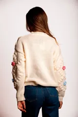 Saco de punto color rojo, con cuello polo y cierre frontal de botones blancos. Presenta flores bordadas en relieve de diferentes colores (azul, amarillo, verde, naranja, rosado) y mangas largas con diseño de burbujas.