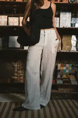 Pantalón de vestir negro de tiro alto, corte recto y pierna ancha. Presenta pliegues frontales y bolsillos laterales.