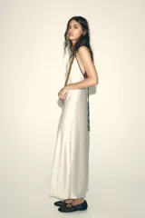Vestido largo color blanco hueso de satén, con escote en V y tirantes finos negros ajustables en la espalda.
