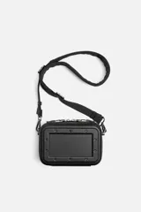 Bandolera rígida negra con formato de caja. Tiene un compartimento principal con cierre de cremallera, un bolsillo interior plano y asa de hombro ajustable y extraíble.