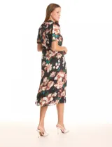 Vestido midi de satén estampado con flores en tonos rosados, blancos y verdes sobre fondo negro. Presenta cuello a la base con frunce, mangas cortas tipo balloon con terminación elastizada, cintura definida y un tajo lateral pronunciado. La espalda cuenta con un lazo para anudar que permite ajustar la caída del cuello. Incluye forro interno a tono.
