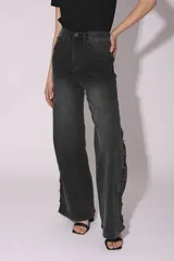 Pantalón de jean gris oscuro con lavado gastado, corte acampanado y tachas plateadas en los laterales.