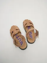 Sandalias de cuero color beige con tiras entrecruzadas, hebilla lateral y suela de goma negra.