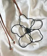 Collar con dije de flor hecho a mano con alambre negro y cordón de gamuza marrón con cuentas plateadas en los extremos.