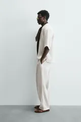 Camisa de lino color blanco, con cuello de solapas de muesca, manga corta y cierre frontal cruzado oculto. Presenta un calce relajado y aberturas laterales en el bajo.