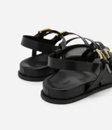 Sandalias negras con tiras de cuero sintético, suela plana y hebillas doradas.