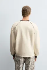 Sudadera color crema de corte relaxed fit, con cuello redondo y manga larga. Presenta un estampado en el frente con la palabra "ULTRAVEX" en letras negras y la palabra "FUTURIO" debajo.