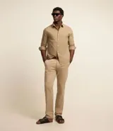 Pantalón de vestir color beige, de corte recto, con cintura fija con trabillas, cierre por cremallera y botón, y bolsillos laterales y traseros.