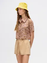 Camisa crop verde con estampado abstracto en tonos naranja y celeste, de mangas cortas y cuello camisero. Confeccionada en viscosa.