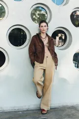 Cazadora bomber de cuero color marrón, con cuello alto, manga larga y bolsillos de parche con solapa en el delantero. Cierre frontal con cremallera metálica y botones a presión ocultos por solapa.