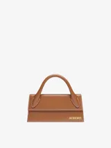 Bolso de mano color marrón, de cuero, con asa corta reforzada, cierre magnético y correa ajustable extraíble. Tiene un bolsillo interior, logotipo y herrajes metálicos dorados.