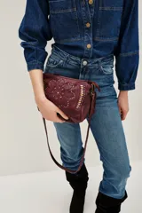 Cartera de cuero vacuno color bordó con diseño floral grabado y apliques de tachas doradas y plateadas en el frente. Posee correa larga para llevar al hombro o cruzada.