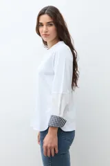Remera blanca de manga larga con puños doblados que muestran un estampado vichy (cuadros) en azul marino y blanco. Tiene cuello redondo y un calce relajado.