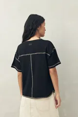 Remera blanca de algodón liviano, de manga corta y cuello redondo. Presenta costuras a contratono visibles en hombros y mangas.