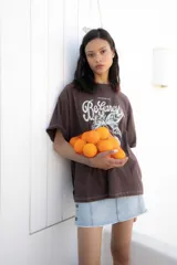 Remera marrón de corte amplio con estampado de texto y dibujo en color blanco.