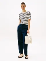 Cartera tote color crema con doble asa de mano y correa larga de tela ajustable y removible. Tiene un monedero extraíble con cierre y logo en relieve, cierre magnético y el monograma TH en la parte delantera.