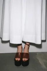 Sandalias de cuero color marrón con plataforma de cuña de madera oscura y correa de tobillo ajustable con hebilla dorada.