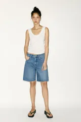 Bermuda de denim azul de tiro medio con cinco bolsillos, trabilla ajustable en la espalda, bajo sin costuras y cierre frontal con botones metálicos.