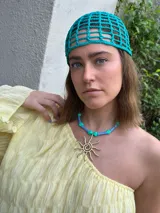 Collar con cadena de cuentas azules y verdes, y dije de sol dorado.
