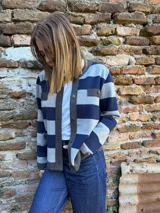Chaqueta tejida de lana a rayas horizontales grises y azul marino, con cuello redondo, cierre frontal con botones dorados y bolsillos frontales con solapa.