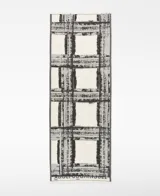 Chal de algodón orgánico con estampado a cuadros en blanco y negro, con efecto pincelada y bordes desflecados. Presenta el logo estampado en la parte inferior.