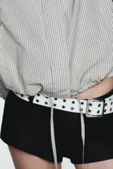 Chaqueta corta de nylon con cuello alto, manga larga y bajo ajustable con cordones. Presenta un estampado de cuadros pequeños en tonos claros.