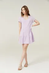 Vestido corto lila con cuello en V y mangas cortas. Tiene corte holgado y dos volados en la falda.