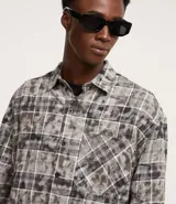 Camisa masculina de franela con estampa de cuadros en tonos grises y blancos, cuello inglés, abotonada, manga larga, modelo comfort con bolsillo en el pecho.