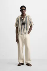 Camisa de crochet color beige con rayas verticales azules, cuello bowling, manga corta y cierre frontal con botones.